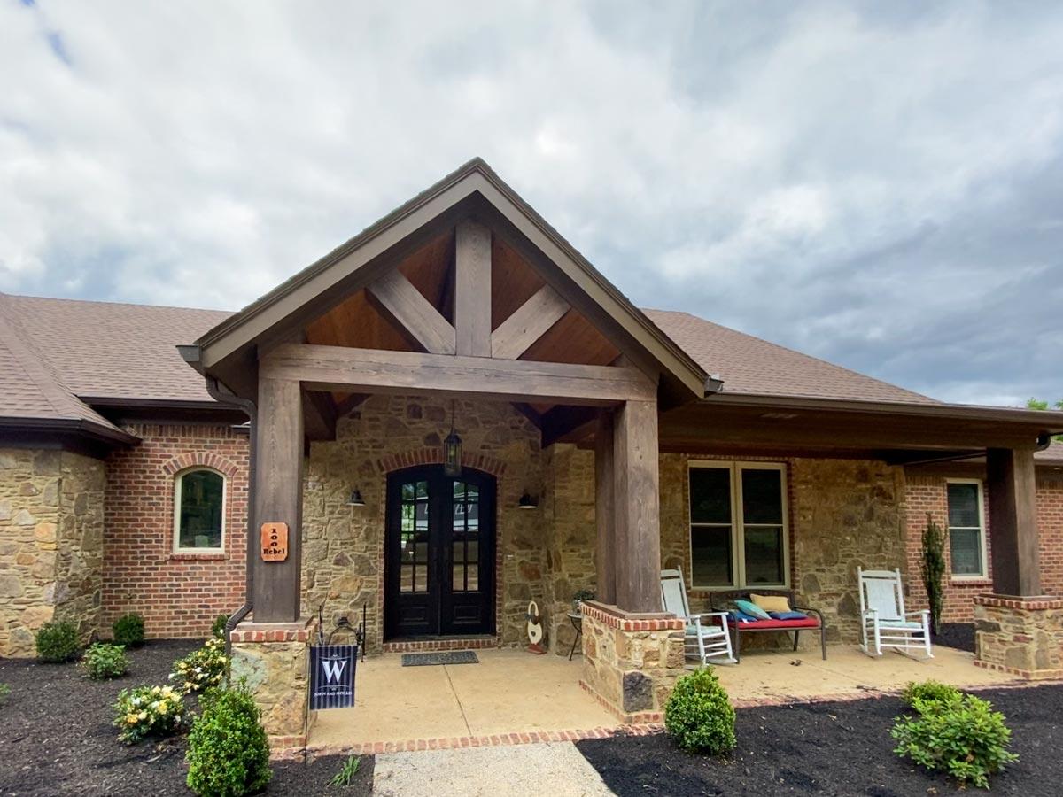House plan exterior: Ranch style with stone and brick facade, covered entry with exposed timber framing, and a front porch with rocking chairs.