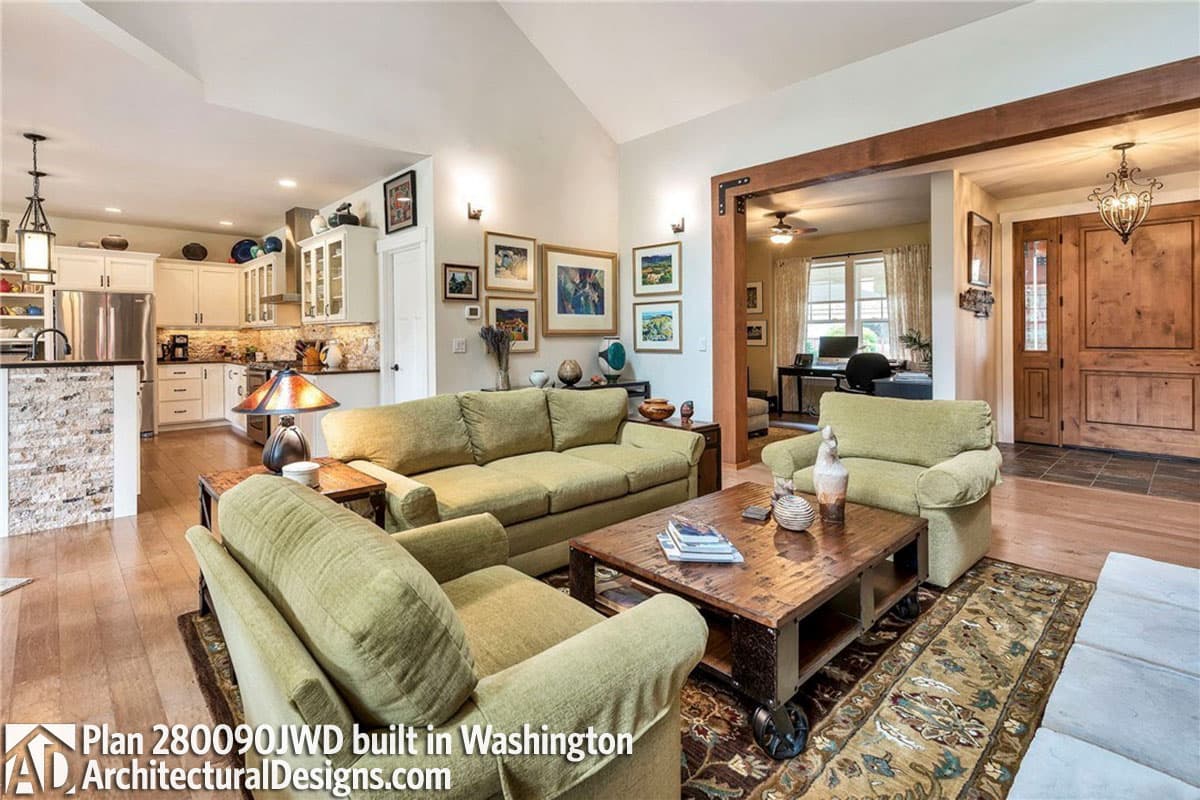 Great room with vaulted ceiling, exposed wood beams, island kitchen, and office area visible through entryway.