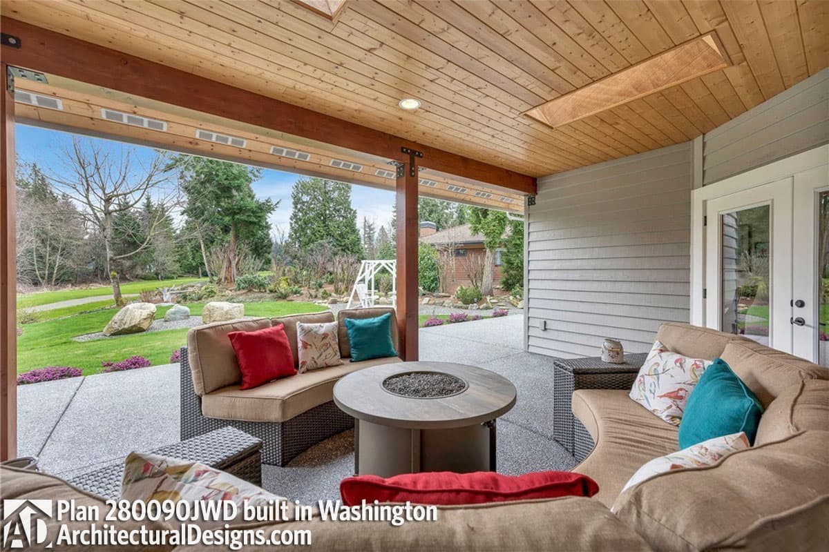 Covered patio with wood ceiling, skylight, fire pit, and seating overlooking landscaped yard.