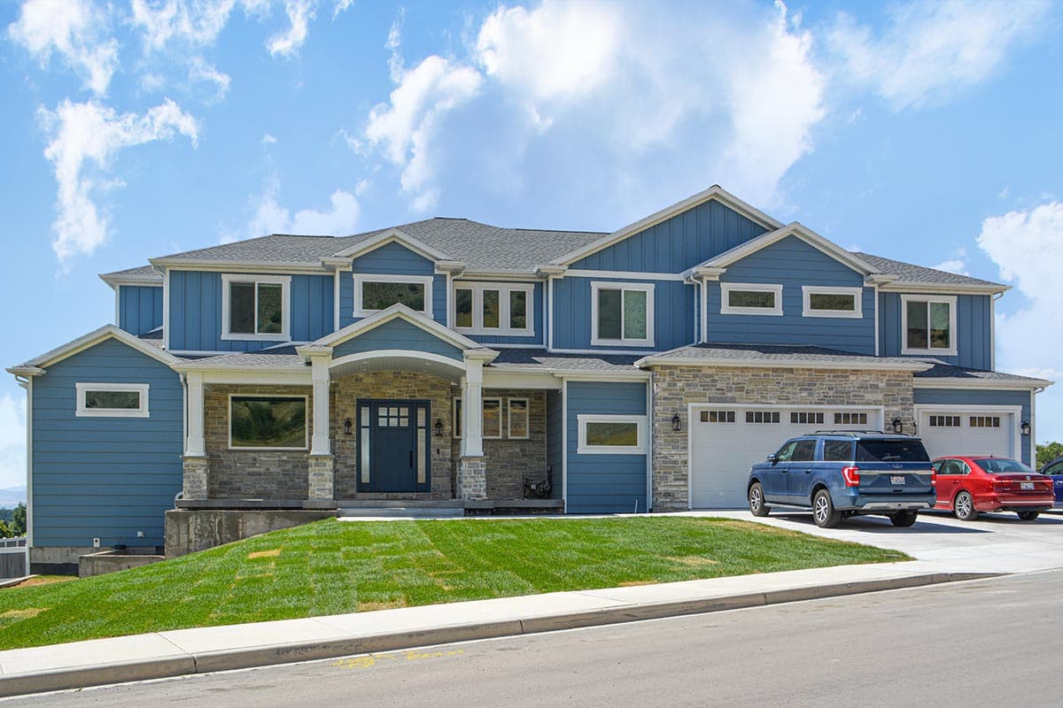 House plan exterior. Two-story home with a gabled roof, stone accents, and a front porch. Features an attached three-car garage.