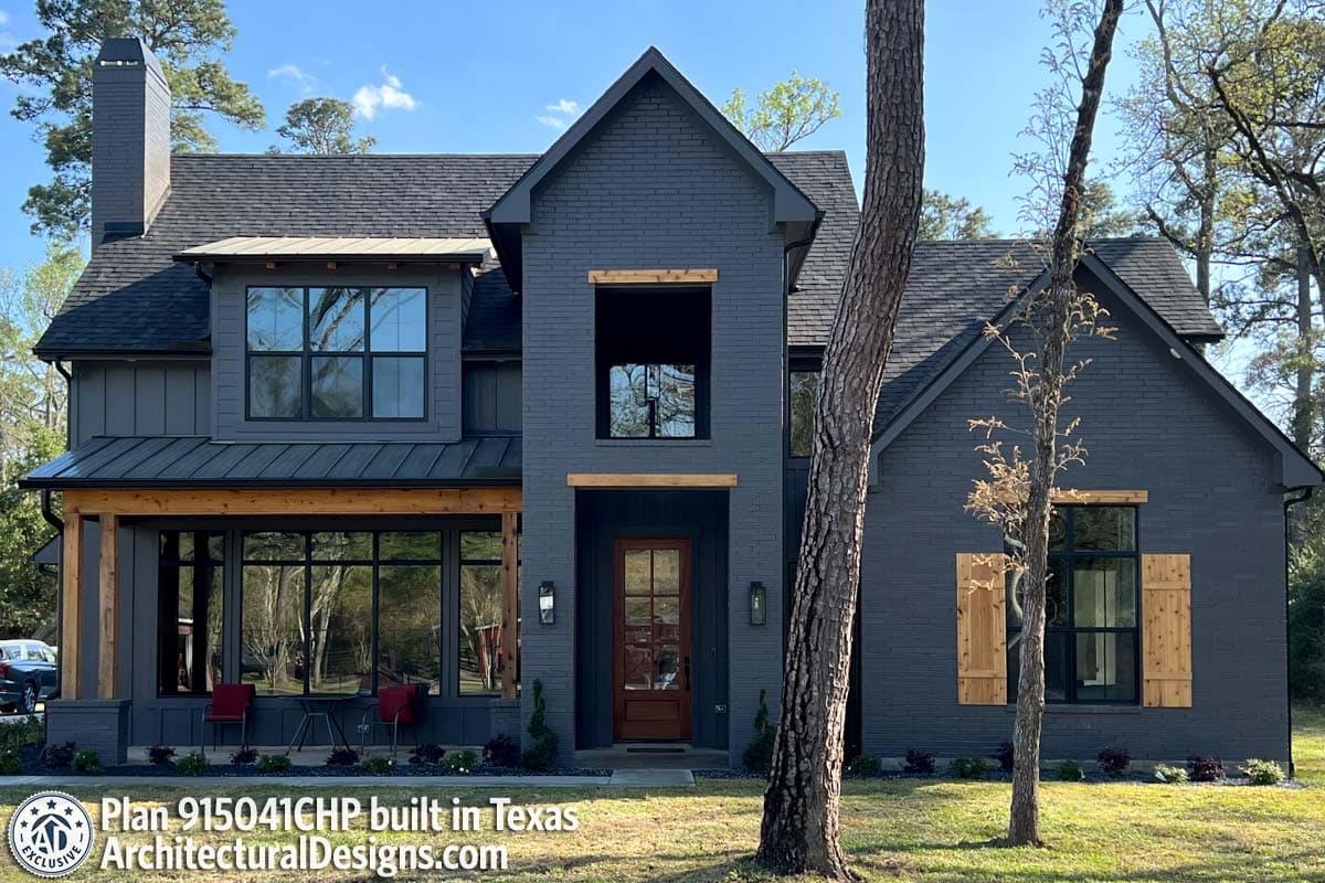 House plan exterior with dark brick, metal roof, wood accents, large windows, and prominent chimney.