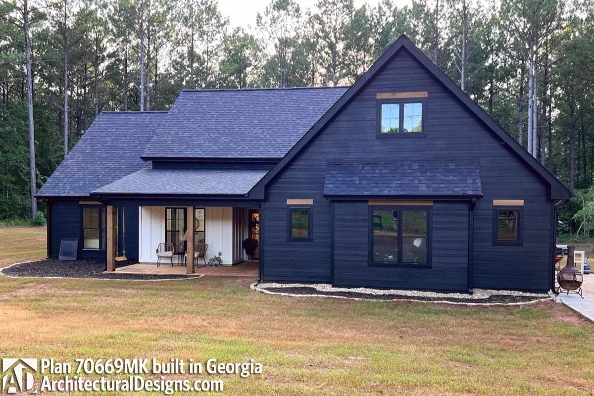 House plan exterior: Modern farmhouse style, dark siding, exposed wood beams, covered front porch with swing and seating.