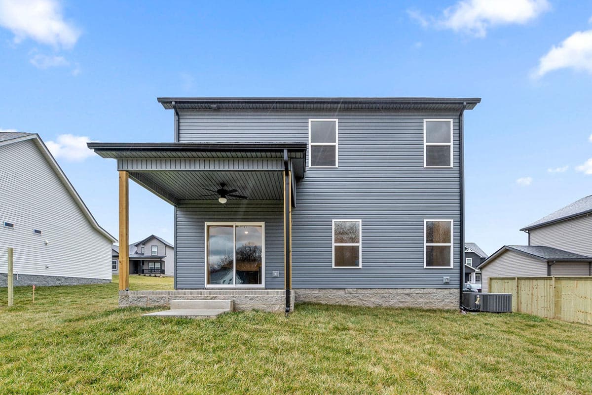 Two-story house exterior with gray siding, covered patio with ceiling fan, and multiple windows.