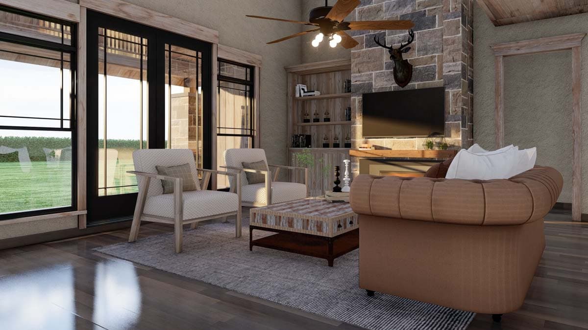 Living room with stone fireplace, wood-paneled bookshelf, and large glass doors. A mounted deer head is above the television.