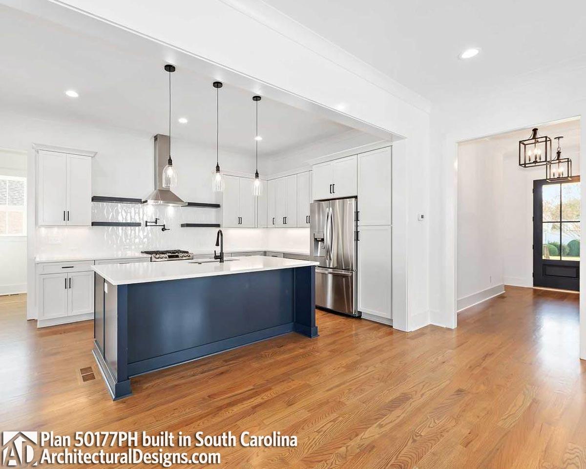 Kitchen with white cabinetry, dark blue island with sink and pendant lights, stainless steel appliances.