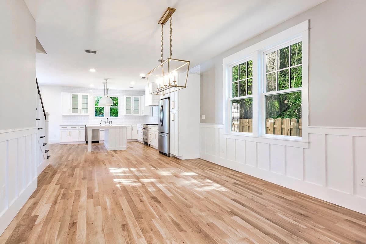 Open-concept kitchen and dining area with white shaker cabinets, a central island, stainless steel appliances, and wainscoting.
