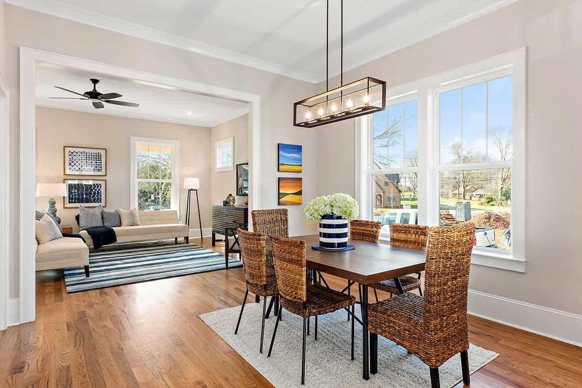 Dining room with wicker chairs around a dark wood table, view into a living room with a sofa and striped rug.