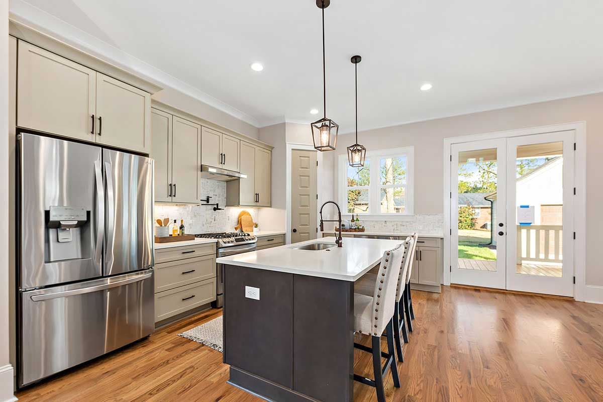 Kitchen featuring a stainless steel refrigerator, island with sink, pendant lights, and double doors leading outdoors.