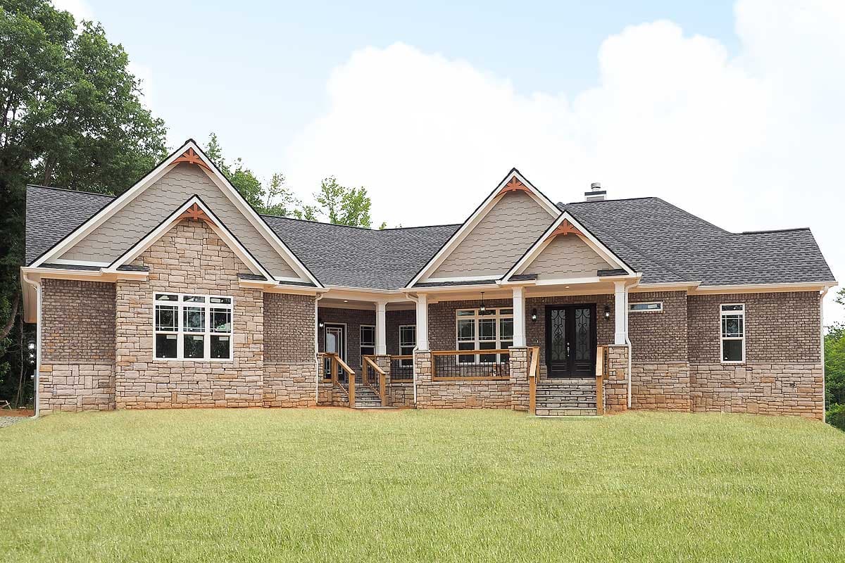 House plan exterior. One-story house with gabled roof, stone and brick facade, and covered porch with supporting columns and railing.