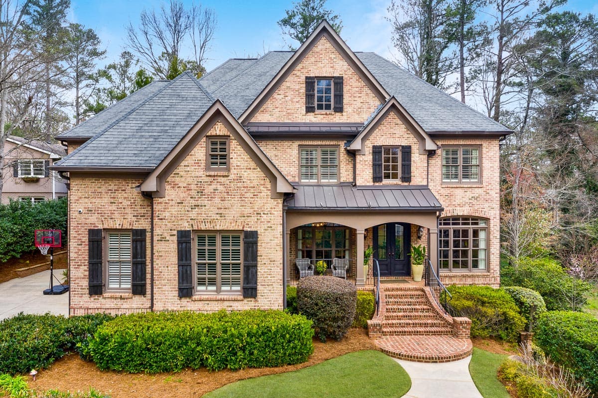 House plan exterior. Two-story brick home with gabled roof, front porch with brick steps, and multiple dormers with shutters.
