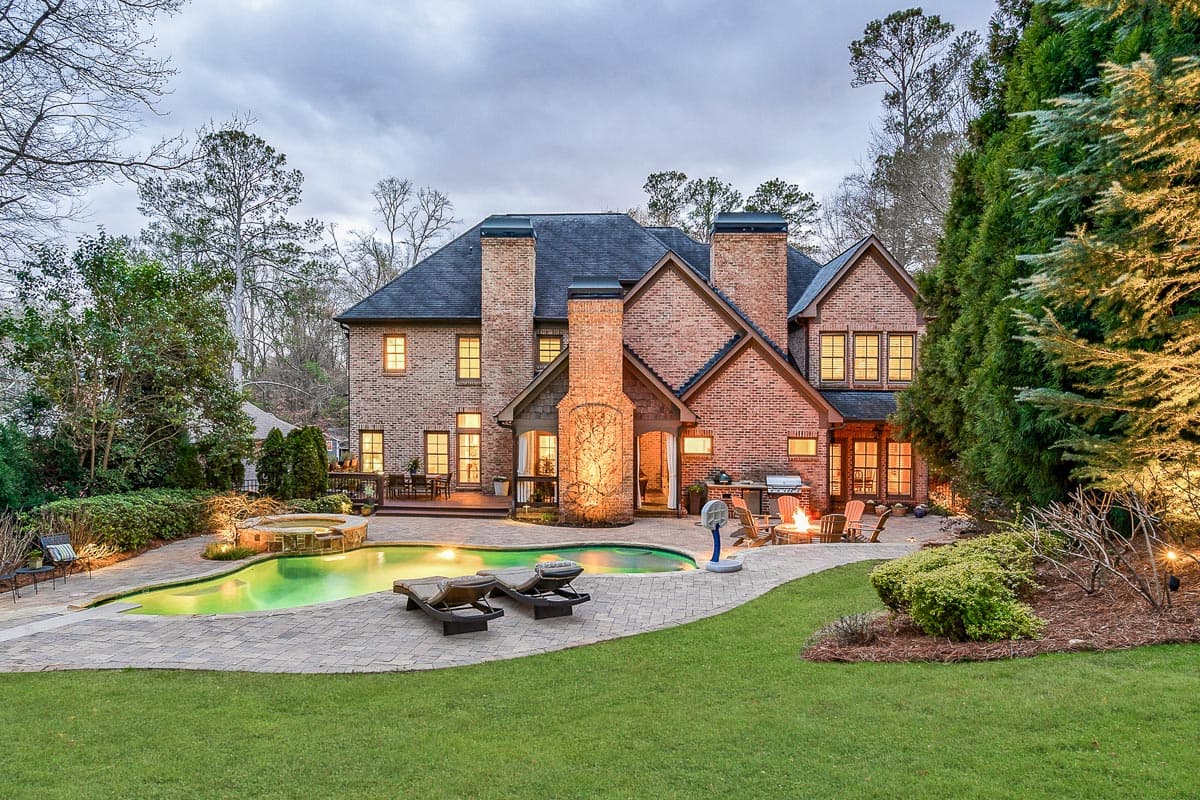 Brick house plan exterior with multiple gables, prominent chimneys, and a pool with a spa and fire pit area.
