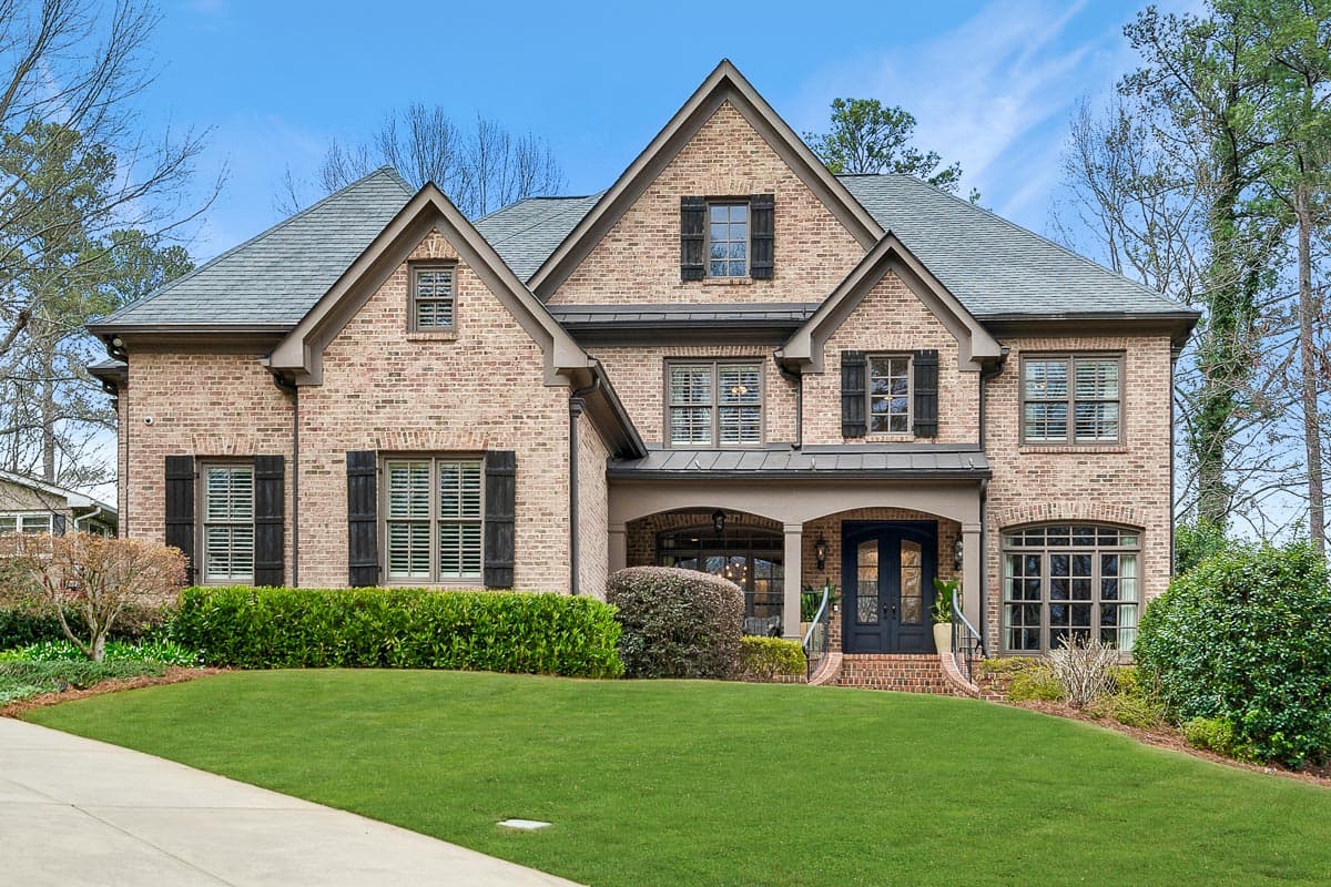 House plan exterior of a two-story brick home with gabled dormers, arched windows, and a covered entry with double doors.