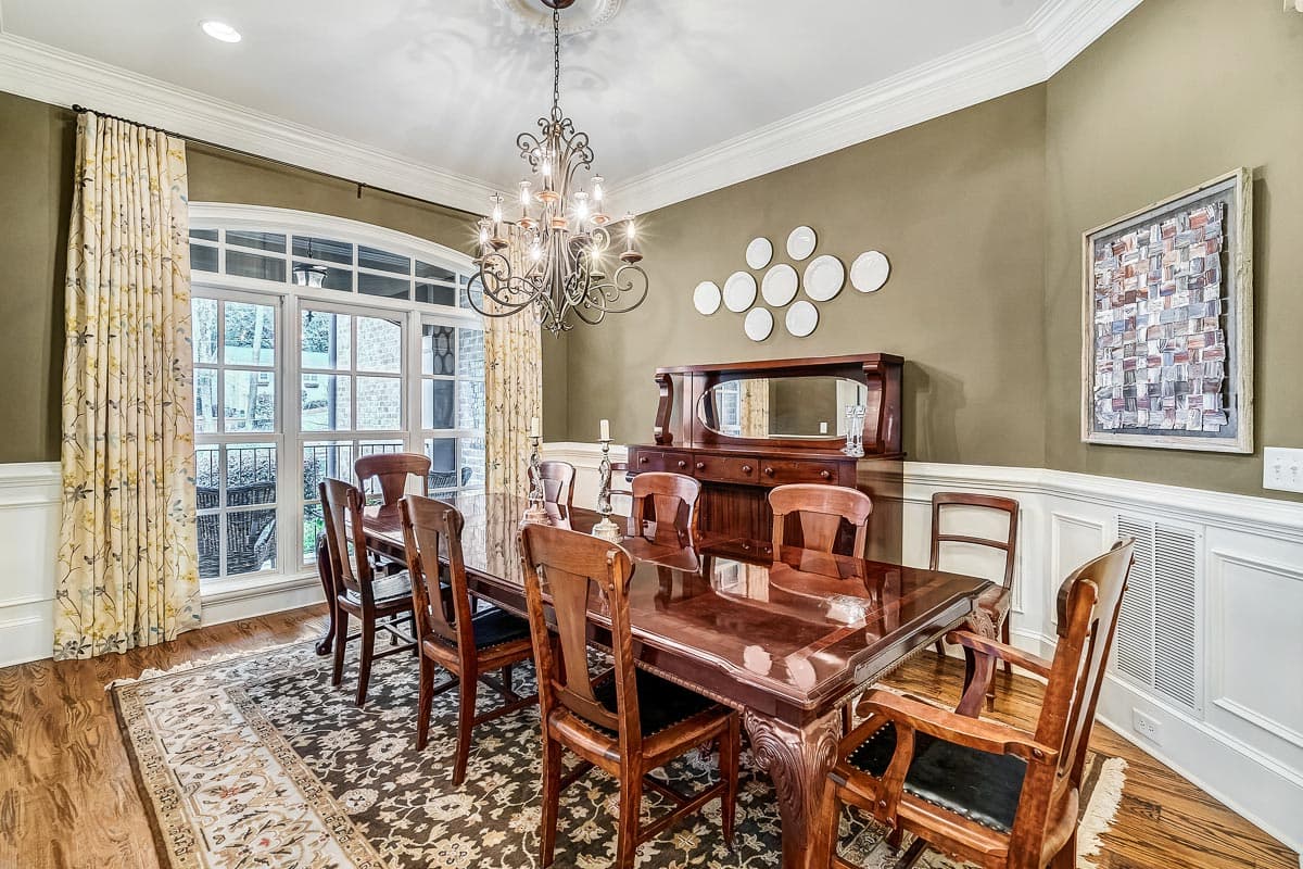 Dining room with dark wood table and chairs, ornate chandelier, buffet, and large arched window.