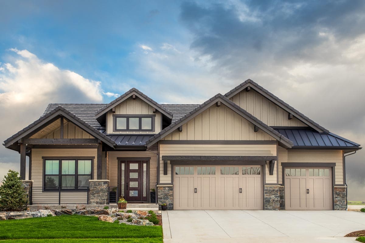 House plan exterior. Craftsman style with a gabled roof, stone accents, and covered porch. Features a three-car garage and multiple dormers.