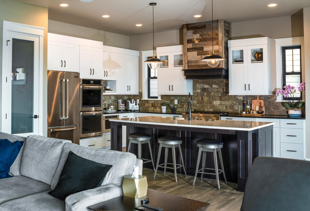 Kitchen with dark island, stainless steel appliances, white cabinetry, and rustic wood range hood.
