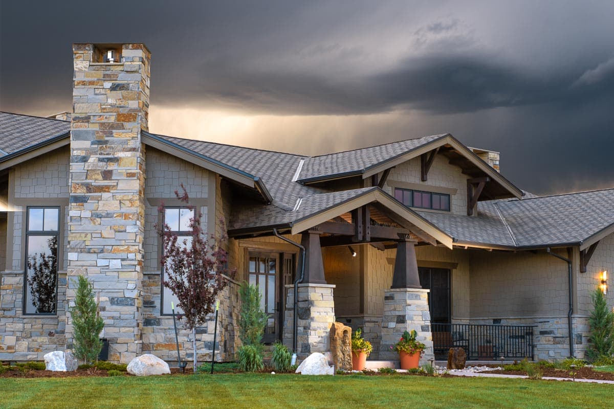 House plan exterior with stone chimney, gabled rooflines, and exposed rafter tails. Craftsman style.