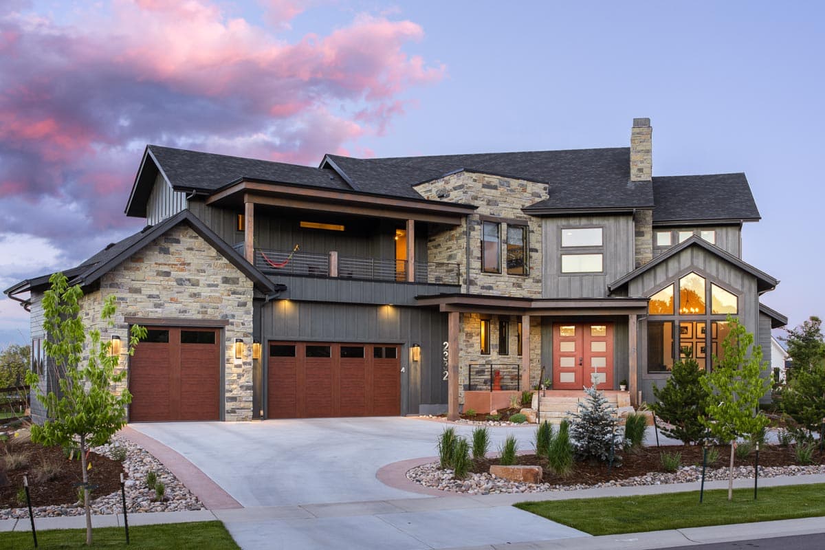 House plan exterior. Two-story with stone facade, multi-gabled roof, covered balcony, and three-car garage.