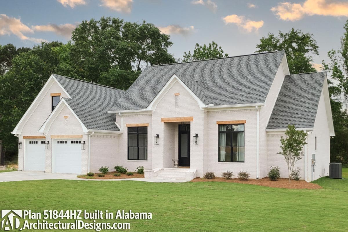 House plan exterior: White brick, single-story home with a gable roof, attached two-car garage, and prominent dormer.