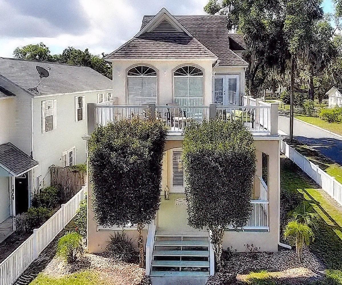House plan exterior: Two-story building with a prominent upper balcony, arched windows, and a central gable.