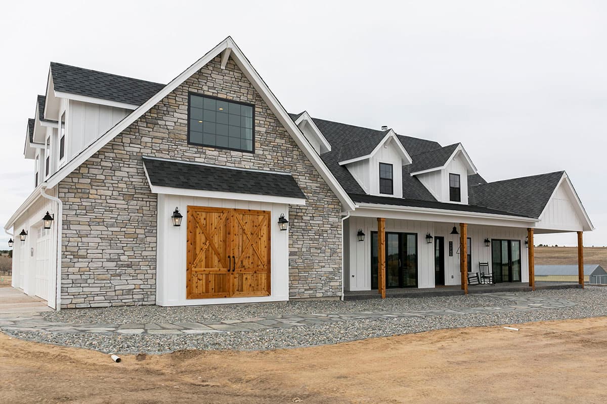 Modern Farmhouse house plan exterior with stone accents, board and batten siding, a covered porch, and a two-car garage with wood doors.