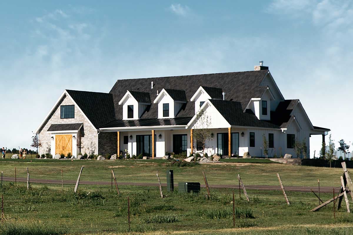 Modern farmhouse house plan exterior with stone accents, gabled dormers, covered porch with wood posts, and a drive-through garage.