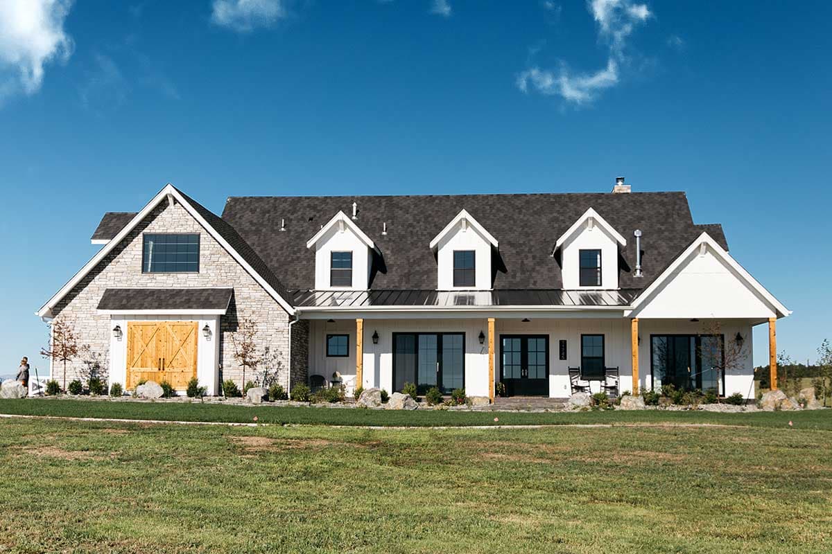 Modern Farmhouse house plan exterior with stone accents, a prominent gable, dormers, and a covered porch with wooden posts.