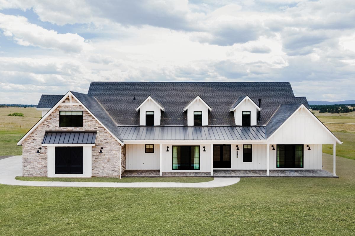 House plan exterior. Modern Farmhouse style with three dormers, stone accent, and covered porch. Features include a metal roof, and gabled rooflines.