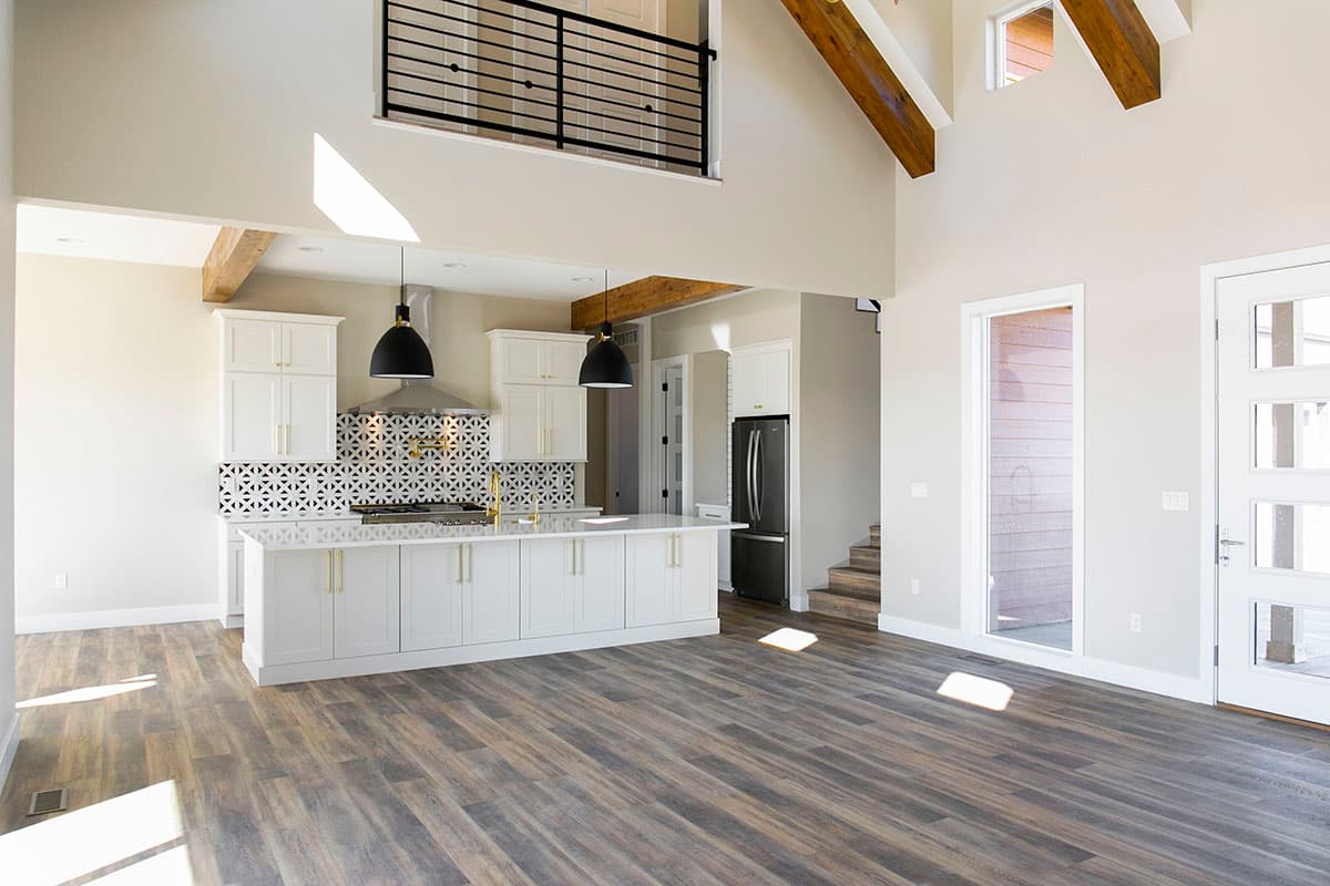Open concept living area with vaulted ceilings, exposed beams, a kitchen island, white cabinetry, and modern pendant lights.