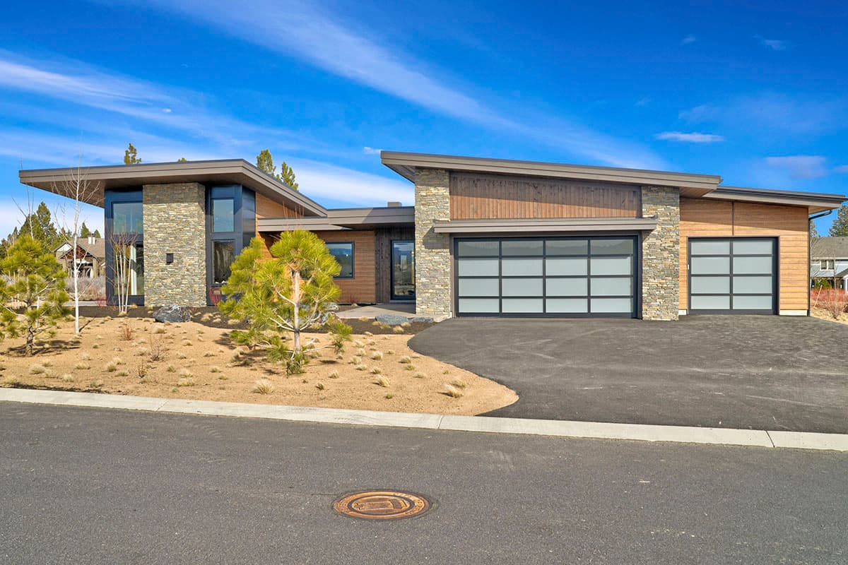 Modern house plan exterior with asymmetrical rooflines, stone and wood siding, and frosted glass garage doors.