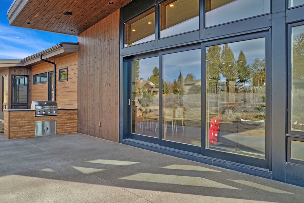 Modern house exterior with vertical wood siding, outdoor kitchen with grill, and large sliding glass doors.