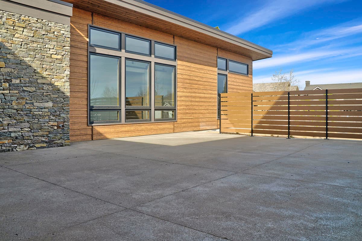Modern house exterior with stone accents, horizontal wood siding, large windows, and slatted fence.