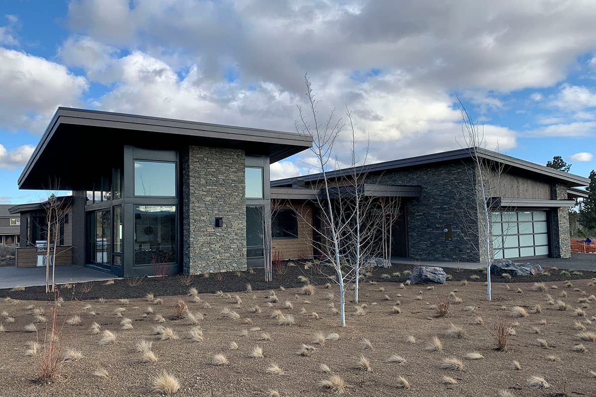 Modern house plan exterior with stone facade, flat rooflines, large windows, and glass garage door.