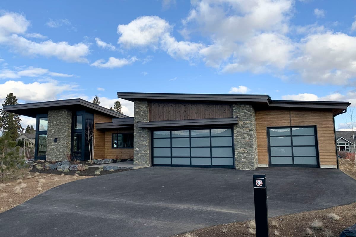 Modern house plan exterior with stone and wood siding, flat rooflines, and frosted glass garage doors.