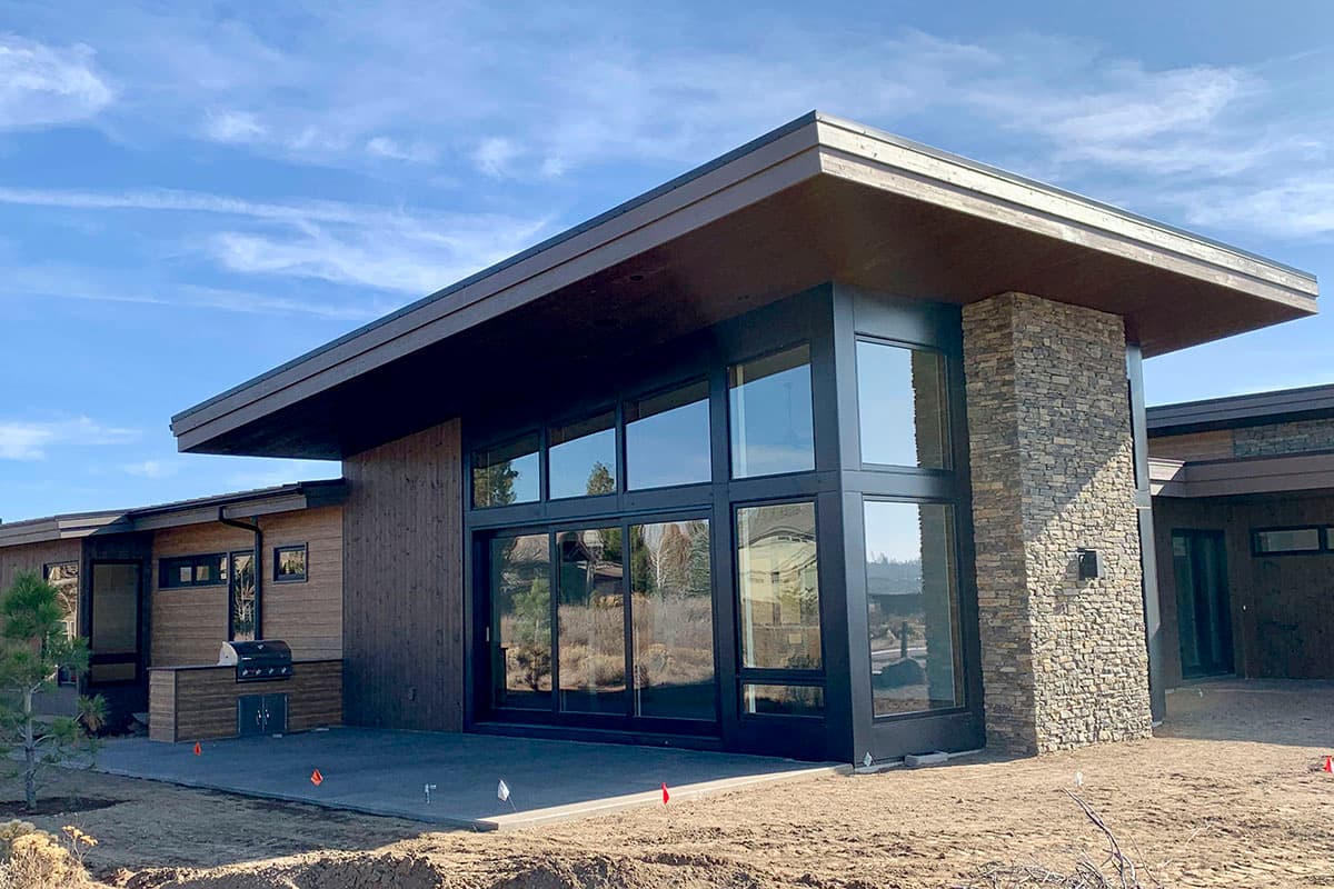 Modern house exterior with wood siding, stone accents, large windows, and a cantilevered roof.