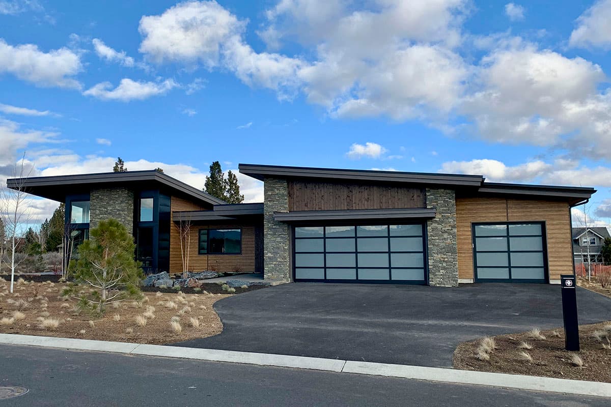 Modern house plan exterior with angled rooflines, wood siding, stone accents, and two frosted glass garage doors.