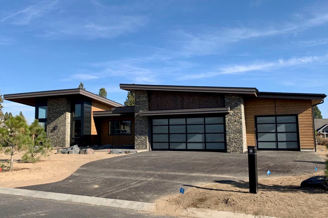 Modern house plan exterior with stone and wood siding, cantilevered rooflines, and two frosted glass garage doors.