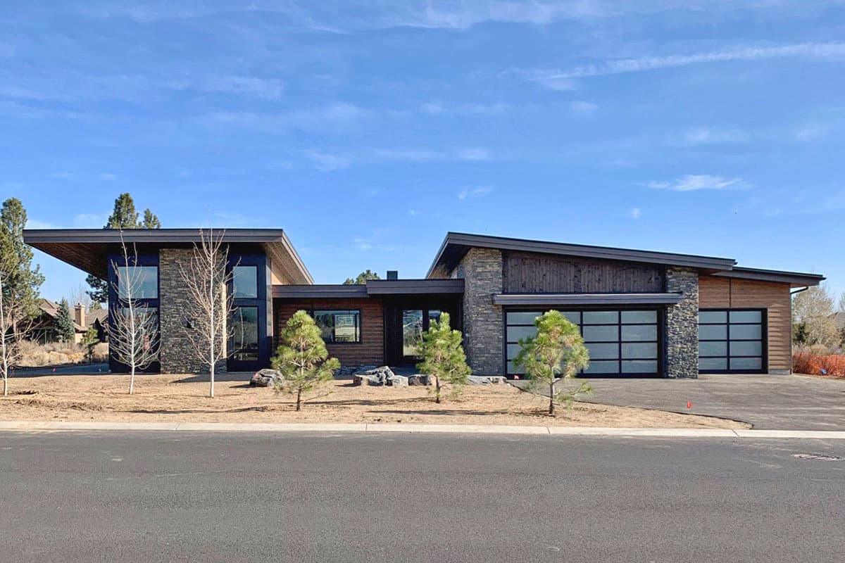 Modern house plan exterior with stone and wood siding, flat rooflines, and glass garage doors.