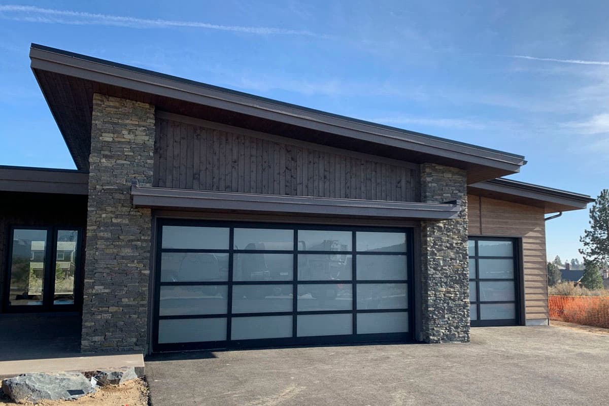 Modern house plan exterior with stone accents, wood siding, and glass garage doors.