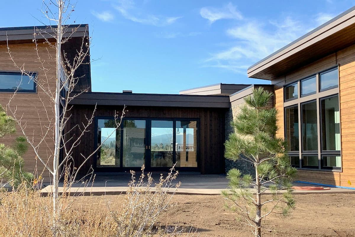 Modern house plan exterior with flat rooflines, wood siding, stone accents, and large glass doors and windows.