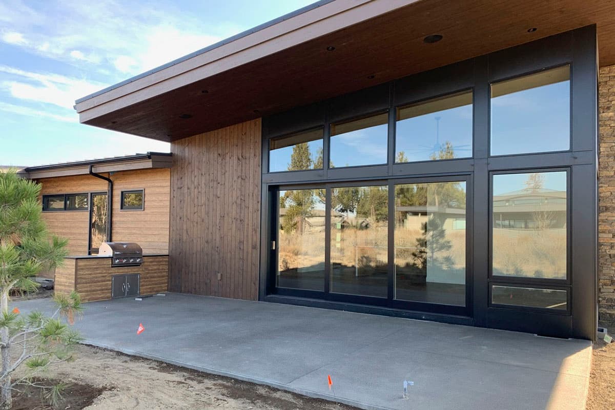 Modern house exterior with wood siding, stone facade, large windows, and built-in outdoor grill.