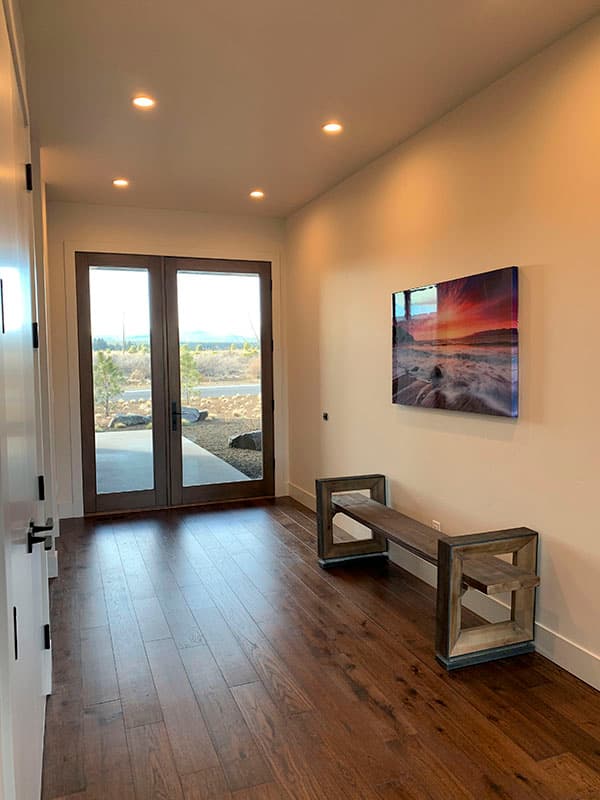Interior view of a hallway with double doors, recessed lighting, hardwood floors, and a bench.