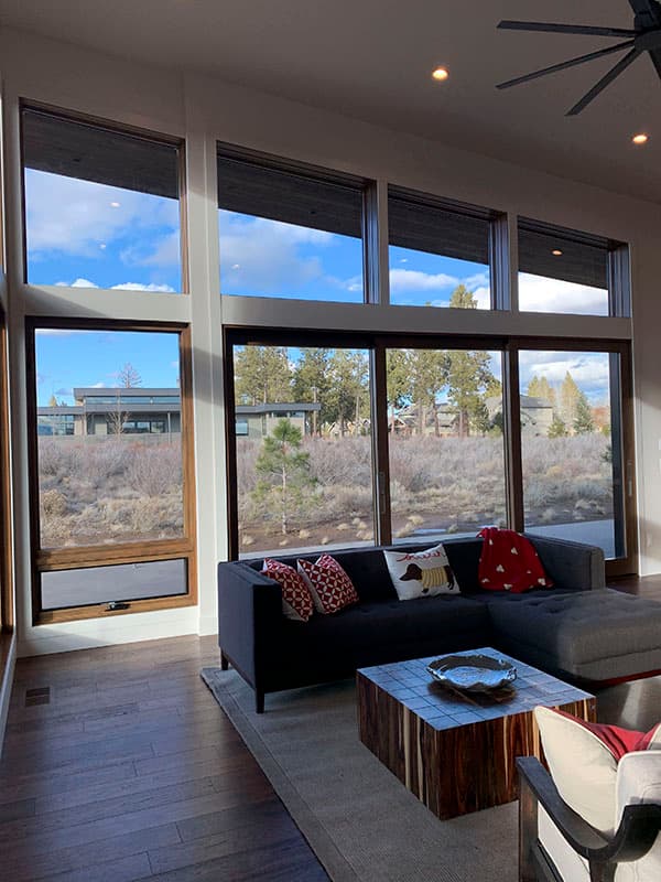 Modern living room with sectional sofa, wood flooring, and large floor-to-ceiling windows offering outdoor views.