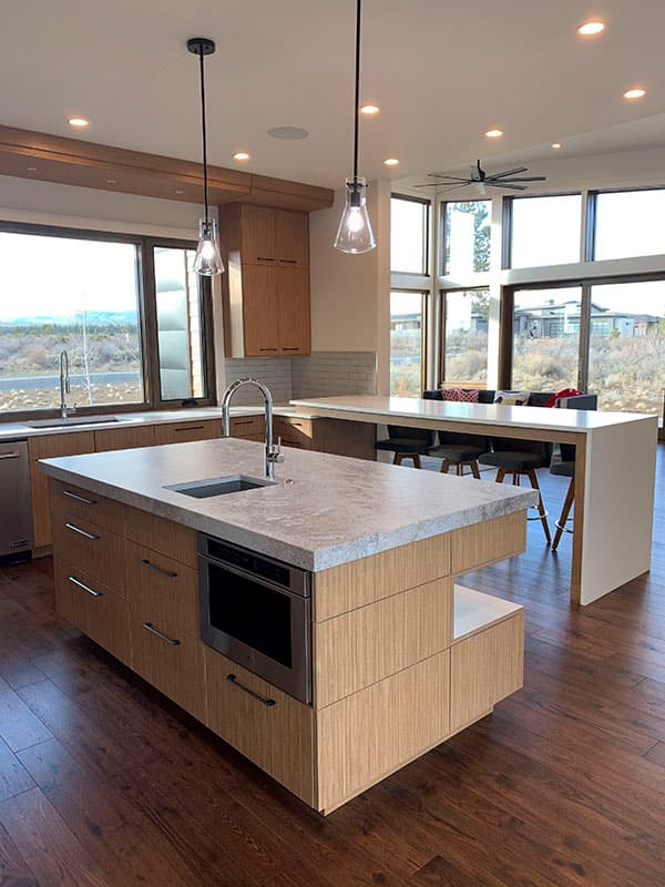 Modern kitchen with large island, integrated microwave, and ample natural light from floor-to-ceiling windows.