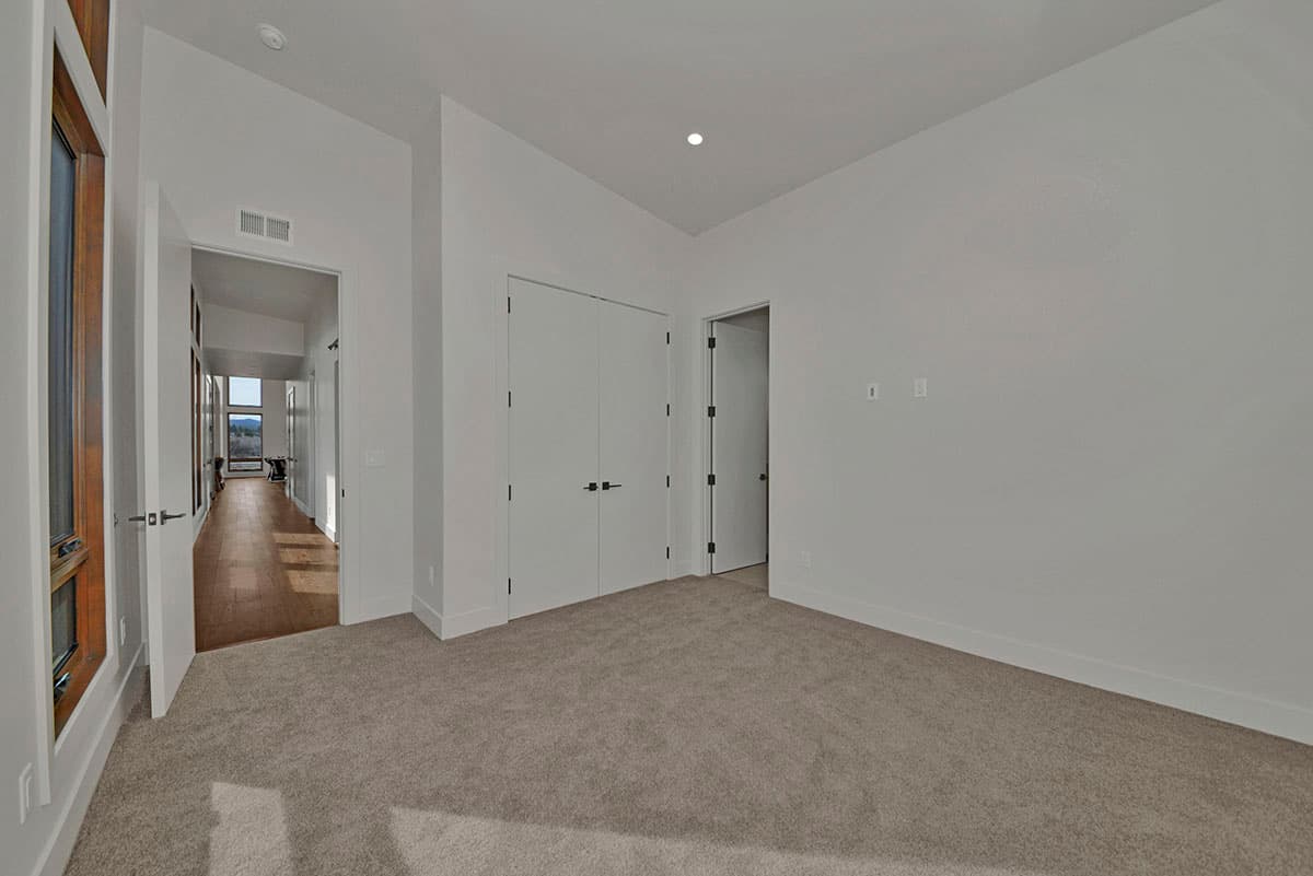 Interior view of a modern house, showing a hallway with wood floors, large windows, and doors to rooms.