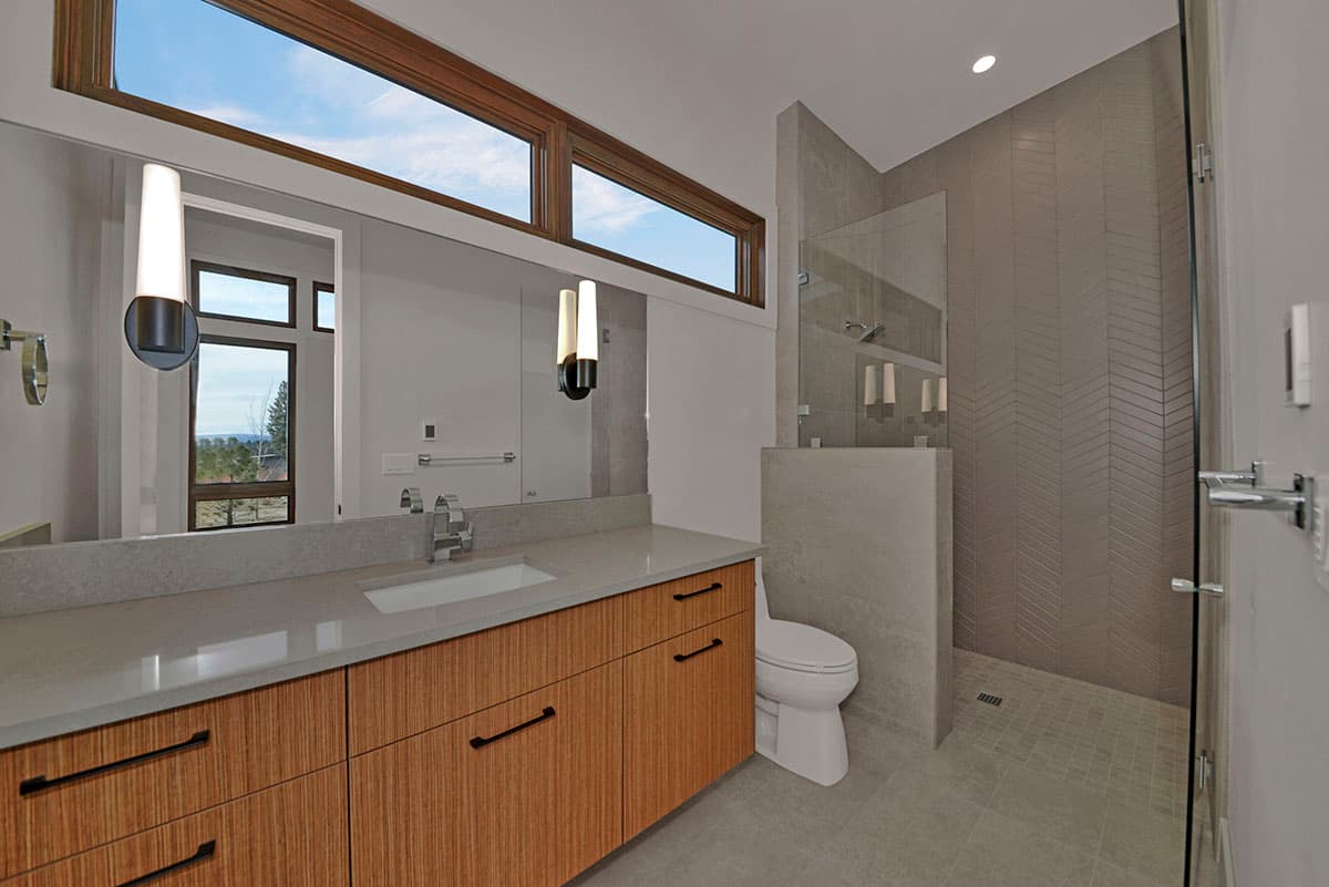Modern bathroom with wood vanity, stone countertop, dual sinks, and walk-in shower with herringbone tile.