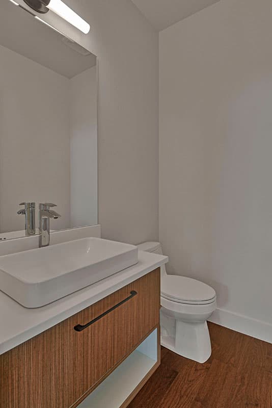 Powder room with vessel sink, wood vanity with modern hardware, and toilet. Accent lighting above mirror.