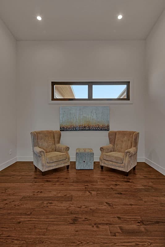 Interior rendering of a seating area with two wingback chairs, ottoman, modern art, and a narrow horizontal window.