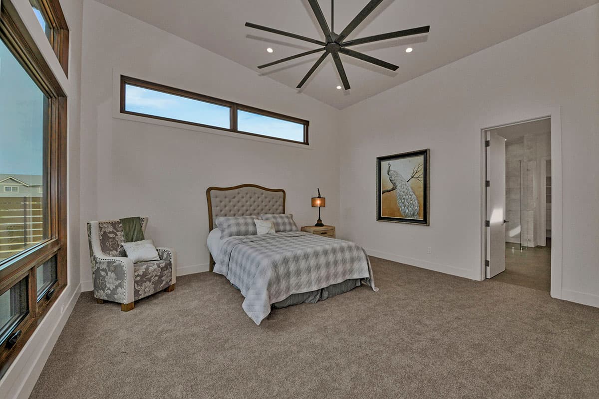 Bedroom with tufted headboard, large corner window, horizontal transom windows, and a starburst ceiling fan.