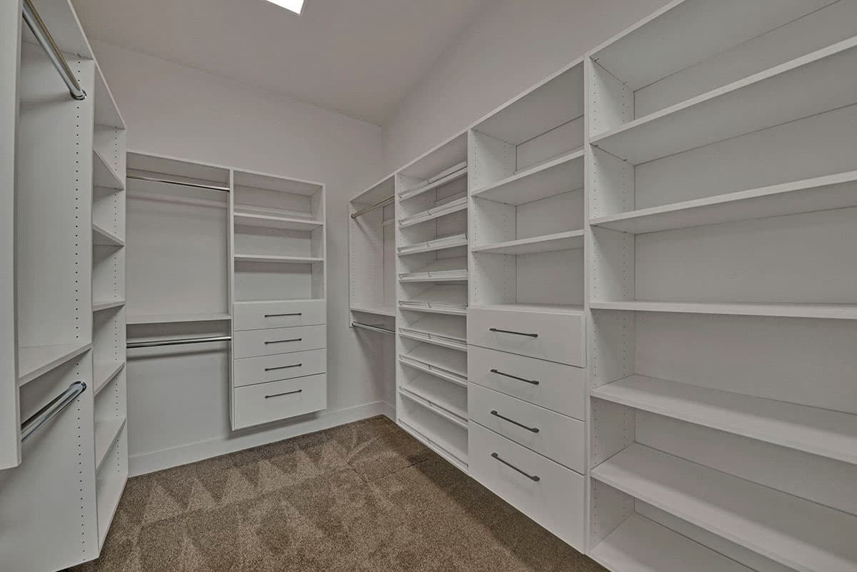 Walk-in closet with white shelving units, drawers, and hanging rods. Sloped ceiling with skylight.