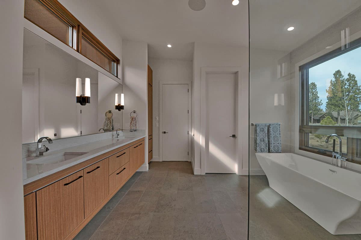 Modern bathroom with double vanity, freestanding tub, and large window with outdoor view.